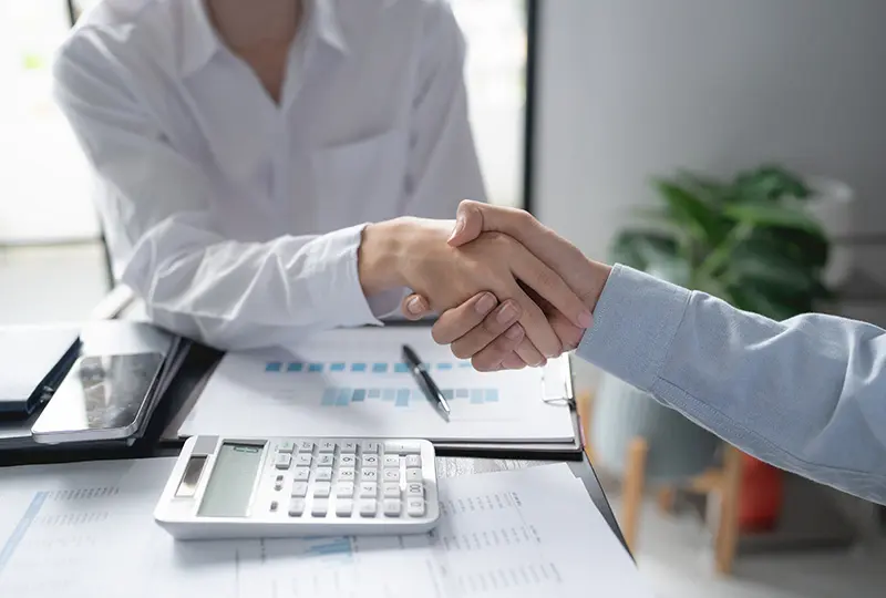 Handshake over desk with documents and calculator.