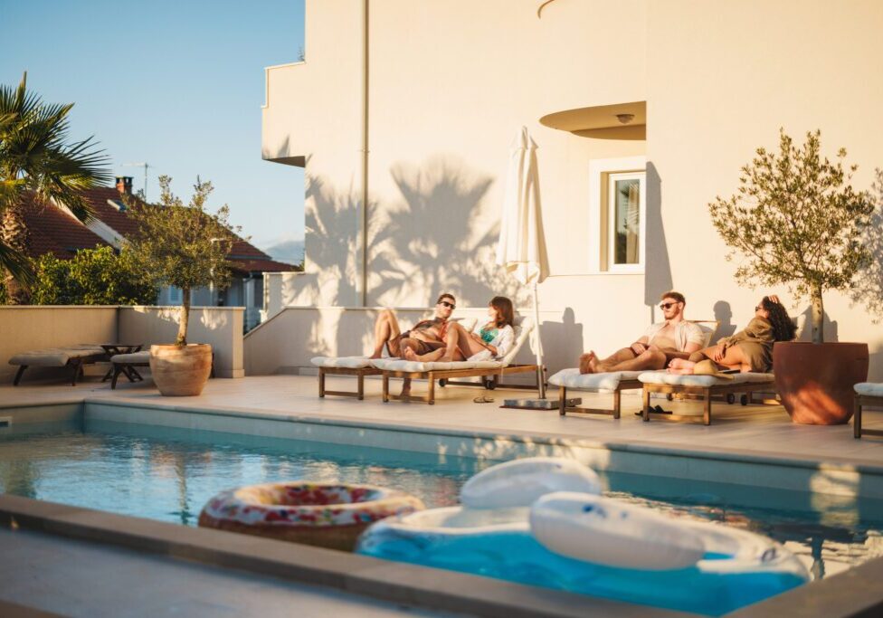 A group of friends enjoys a warm day lounging by a beautiful pool at a tourist resort. The scene captures relaxation, summer vibes, and the joy of friendship in an idyllic outdoor setting.