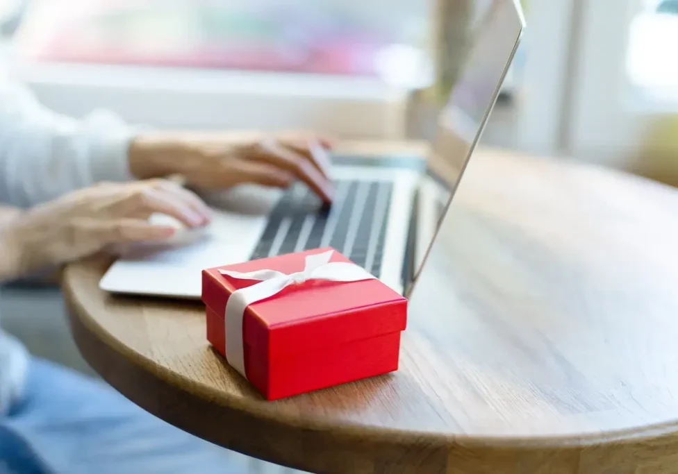 Red gift box near person using laptop.