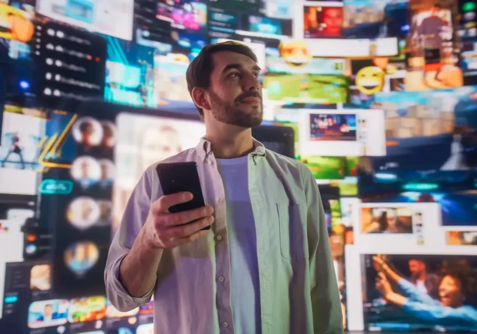 Man holding smartphone, surrounded by digital screens.